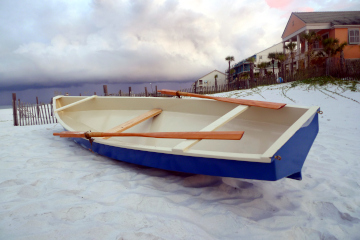 A blue rowboat on a sand dune overlooking the Gulf of Mexico with clouds overhead and colorful beach houses in the background