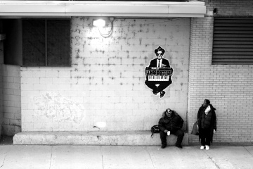 Two people on a Chicago sidewalk under graffiti of someone in a black suit wearing sunglasses and holding a Moog keyboard